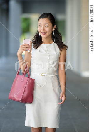 businesswoman walking listening to music via smartphone businesswoman walking listening to music via smartphone 65728031