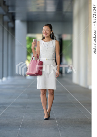 businesswoman walking listening to music via smartphone businesswoman walking listening to music via smartphone 65728047