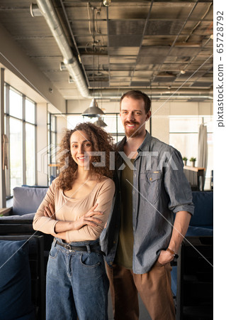 Young cheerful couple in casualwear looking at you while waiting for guests 65728792