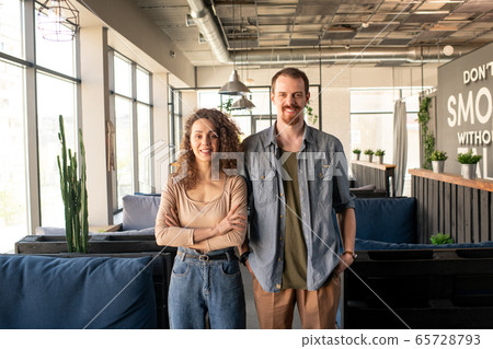 Happy young owners of new contemporary restaurant standing between couches 65728793