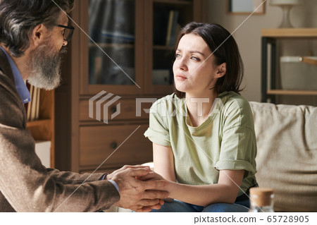 Young unhappy brunette female sitting in front of aged professional psychologist 65728905
