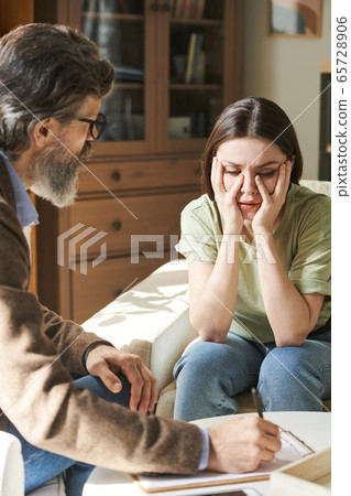 Young worried female patient of psychologist sitting in front of senior man Young worried female patient of psychologist sitting in front of senior man 65728906