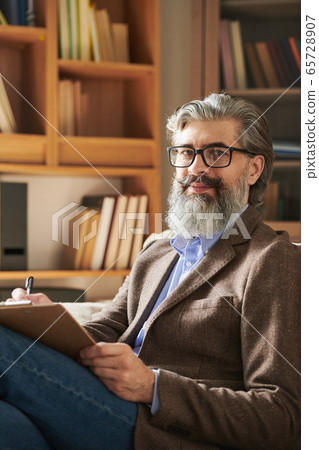 Aged successful psychologist in eyeglasses and smart casualwear looking at you Aged successful psychologist in eyeglasses and smart casualwear looking at you 65728907