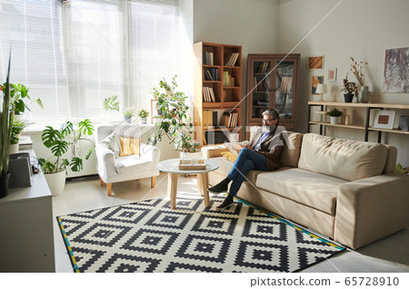Contemporary senior professional psychotherapist sitting on couch by table 65728910