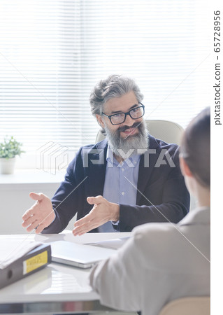 Mature successful businessman in formalwear looking at young applicant 65728956