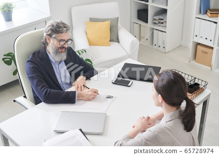 Contemporary employer in formalwear making notes in resumer of new applicant 65728974