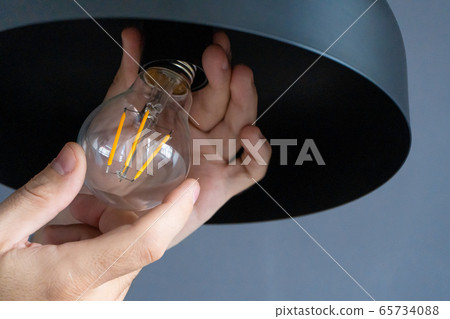 Close-up. A hand changes a light bulb in a stylish Close-up. A hand changes a light bulb in a stylish 65734088