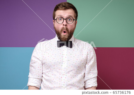 Cute man in round glasses is surprised, he shockedly opened mouth and looks with big eyes. Cute man in round glasses is surprised, he shockedly opened mouth and looks with big eyes. 65736176