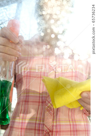 Woman washes a window glass from dust and dirt, using a spray with detergents and rags, on a sunny Woman washes a window glass from dust and dirt, using a spray with detergents and rags, on a sunny 65736234