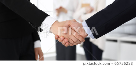 Businessman and woman shaking hands with colleagues at the background. Handshake at meeting in office. Concept of success in business 65736258