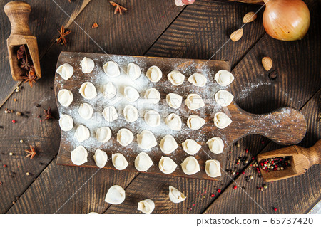 Semi-finished pelmeni dumplings on wooden board Semi-finished pelmeni dumplings on wooden board 65737420