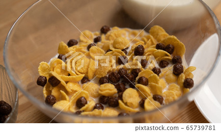 Glass bowl of cornflakes with chocolate balls and milk on light table. Healthy food concept. Quick breakfast concept. Close up shot 65739781