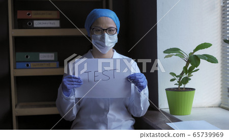 TEST inscription in hands of medical professional. Female docror standing on medical office background near the window. Medical test concept. Coronavirus outbreak concept TEST inscription in hands of medical professional. Female docror standing on medical office background near the window. Medical test concept. Coronavirus outbreak concept 65739969