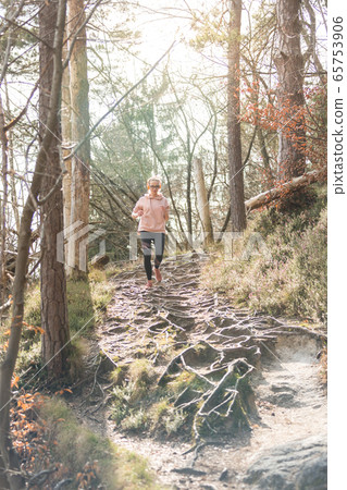 Active sporty woman listening to the music while running in autumn fall forest. Female runner training outdoor. Healthy lifestyle image of young caucasian woman jogging outside 65753906