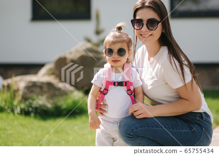 Mom with her adorable little daughter walk in front of house. Happy family spent time outdoors. Mother and daughter in sunglasses 65755434