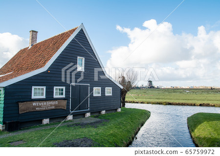 A historic wooden building in the suburbs of Amsterdam, the Netherlands, maintained greenery and a windmill in the distance A historic wooden building in the suburbs of Amsterdam, the Netherlands, maintained greenery and a windmill in the distance 65759972