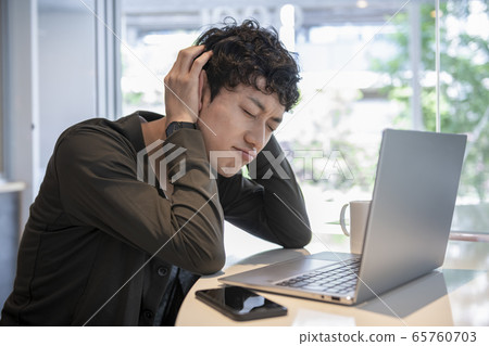 Young man holding his head in front of a laptop Young man holding his head in front of a laptop 65760703
