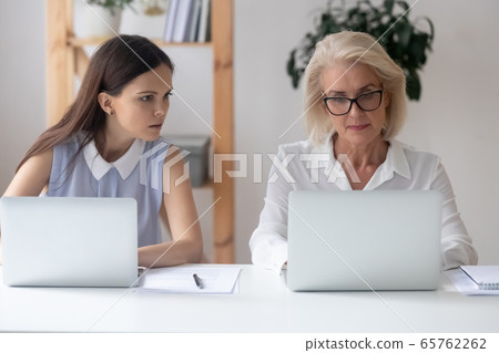 Young female employee peep in colleague laptop 65762262