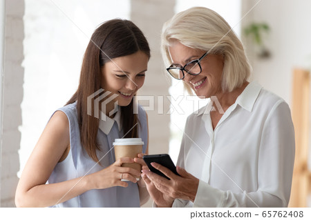 Smiling female colleagues browse smartphone at office coffee break Smiling female colleagues browse smartphone at office coffee break 65762408