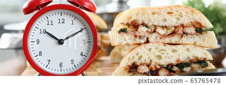 Red alarm clock with sandwich stands on wooden table background Red alarm clock with sandwich stands on wooden table background 65765478