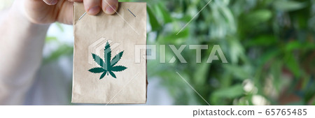 Male hand hold paper packet with marijuana symbol closeup background Male hand hold paper packet with marijuana symbol closeup background 65765485