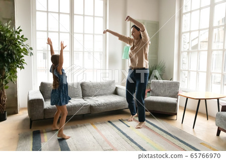 Energetic grandmother dancing in living room with granddaughter 65766970
