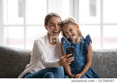 Smiling young mom and little daughter laugh using smartphone 65766997