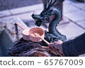 A visitor of a Shinto Shrine is holding water ladle about to purify their hands with water from Chozuya. Dragon sculpture dripping fountain. 65767009