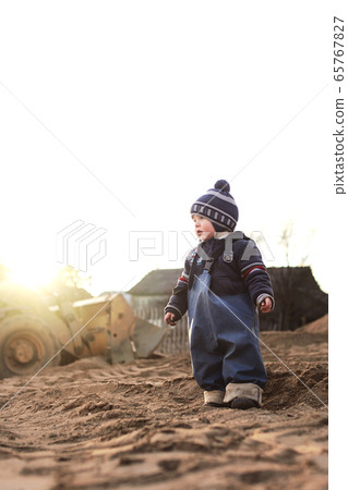 A boy in the village on the background of a tractor walks on the sand . A boy in the village on the background of a tractor walks on the sand . 65767827