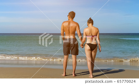 pretty young couple walk along beach to ocean water pretty young couple walk along beach to ocean water 65770024