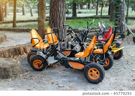 Many modern pedal toy cars for two person fo rent or sharing outdoors in city park, garden or forest. Healthy family outside sport recreation activities. Fun children cycle transport Many modern pedal toy cars for two person fo rent or sharing outdoors in city park, garden or forest. Healthy family outside sport recreation activities. Fun children cycle transport 65770291