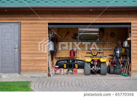 Facade front view open door ATV quad bike motorcycle parking messy garage building with wooden siding at home driveway backyard and lawn path. House warehouse for tools and equipment . Garage sale 65770308
