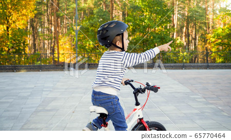 Happy little boy riding his biyccle and pointing with index finger Happy little boy riding his biyccle and pointing with index finger 65770464