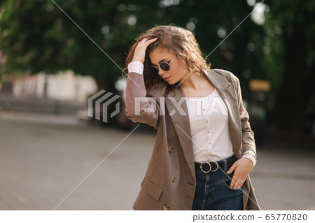 Portrait of attractive woman with curly hair in sunglasses outdoors. Happy young woman walking in the city Portrait of attractive woman with curly hair in sunglasses outdoors. Happy young woman walking in the city 65770820