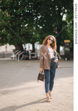 Portrait of attractive woman with curly hair in sunglasses outdoors. Happy young woman walking in the city Portrait of attractive woman with curly hair in sunglasses outdoors. Happy young woman walking in the city 65770826