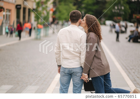 Back view of Happy couple walking in the city. Attractive young woman and handsome young man in centre of the city. Smiled people Back view of Happy couple walking in the city. Attractive young woman and handsome young man in centre of the city. Smiled people 65770851