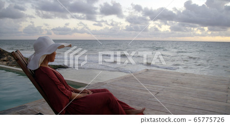 Beautiful young woman sits by the ocean taking in sunset while on vacation 65775726