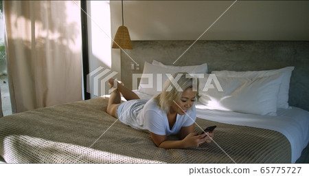 Cute woman on bed happy and excited to hear from her friend while on vacation Cute woman on bed happy and excited to hear from her friend while on vacation 65775727