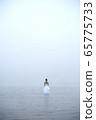 Woman in white dress and blue hair looks as if she is drifting by water surrounded by mist and fog  65775733