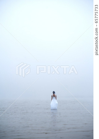 Woman in white dress and blue hair looks as if she is drifting by water surrounded by mist and fog  65775733