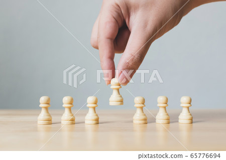 Successful business team leader concept. Hand chooses a wooden chess standing out from the crowd Successful business team leader concept. Hand chooses a wooden chess standing out from the crowd 65776694