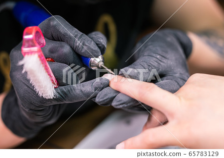 Process manicure close-up. Preparation for hardware manicure. Beautician in rubber gloves cuts the cuticle and processes nails. Process manicure close-up. Preparation for hardware manicure. Beautician in rubber gloves cuts the cuticle and processes nails. 65783129