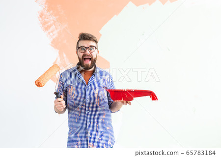 Funny man painting interior wall of home with paint roller. Redecoration, renovation, apartment repair and refreshment concept. Funny man painting interior wall of home with paint roller. Redecoration, renovation, apartment repair and refreshment concept. 65783184