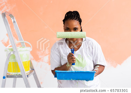 Happy smiling african american woman painting interior wall of new house. Redecoration, renovation, apartment repair and refreshment concept. Happy smiling african american woman painting interior wall of new house. Redecoration, renovation, apartment repair and refreshment concept. 65783301
