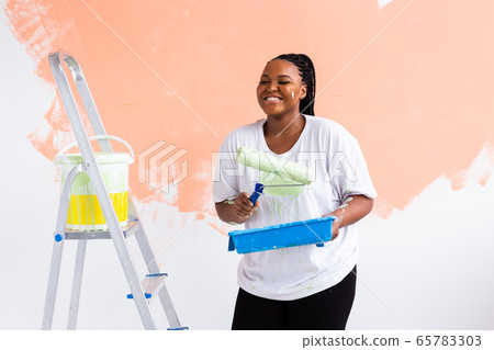 Lovely african american housewife painting wall. Renovation, redecoration and repair concept. Lovely african american housewife painting wall. Renovation, redecoration and repair concept. 65783303