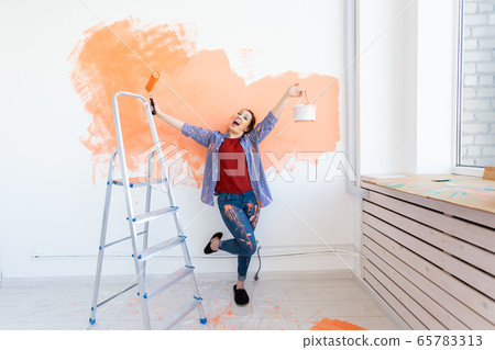 Happy smiling woman painting interior wall of new house. Redecoration, renovation, apartment repair and refreshment concept. 65783313