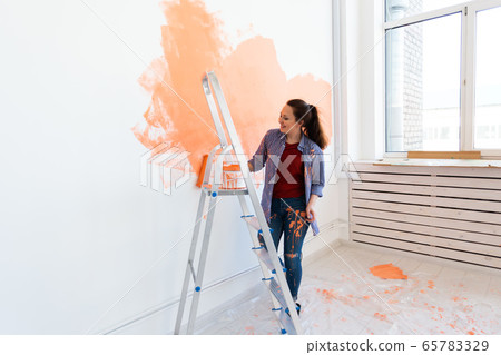 Happy young woman painting wall in her new apartment. Renovation, redecoration and repair concept. Happy young woman painting wall in her new apartment. Renovation, redecoration and repair concept. 65783329