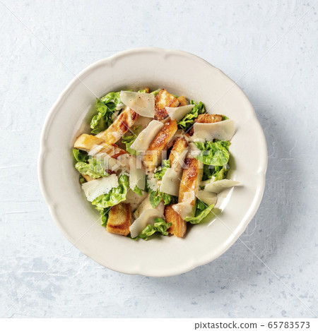 Caesar salad. Grilled chicken breast slices, green romaine salad leaves, croutons and Parmesan cheese, the classic recipe on a white marble background, overhead square shot 65783573