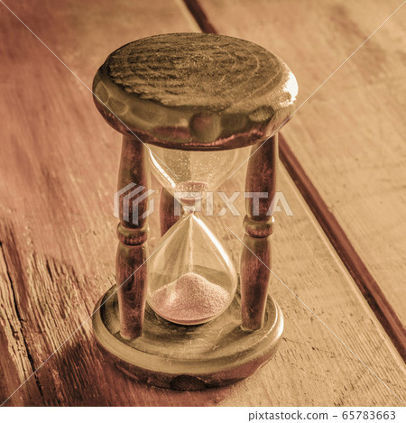 Time concept. A vintage hourglass with sand falling through, on a rustic background, toned square image Time concept. A vintage hourglass with sand falling through, on a rustic background, toned square image 65783663