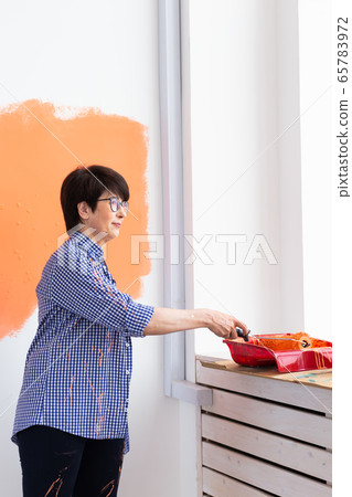 Repair in the apartment. Happy middle-aged woman paints the wall with paint. Repair in the apartment. Happy middle-aged woman paints the wall with paint. 65783972
